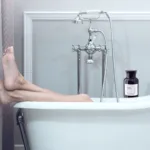 The Twelfth Element Bottle on the side of the bath as a woman stretches out her legs to relax in the bathtub.